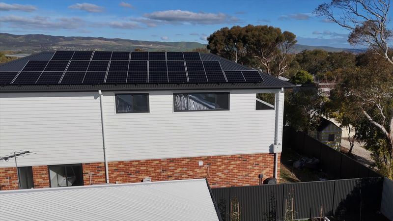 Second-storey addition in white weatherboard with black-framed windows and a solar array, above the original red-brick home, with hills beyond