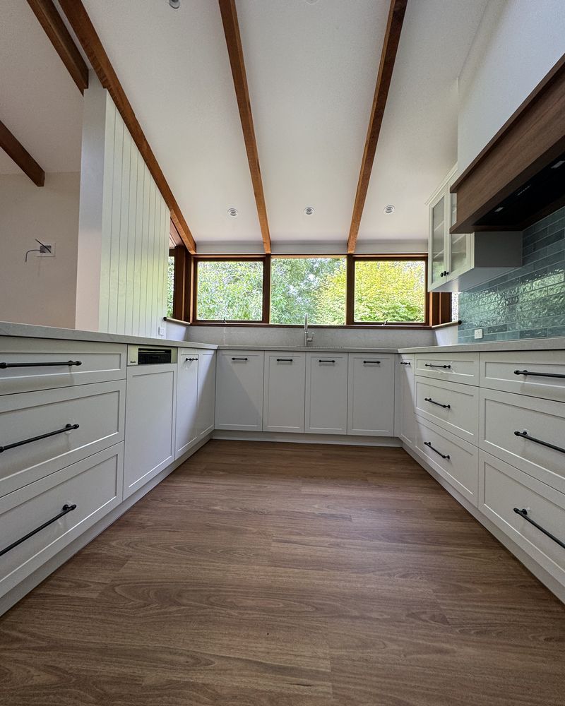White shaker drawers and cabinets running either side of a timber floor towards the garden windows