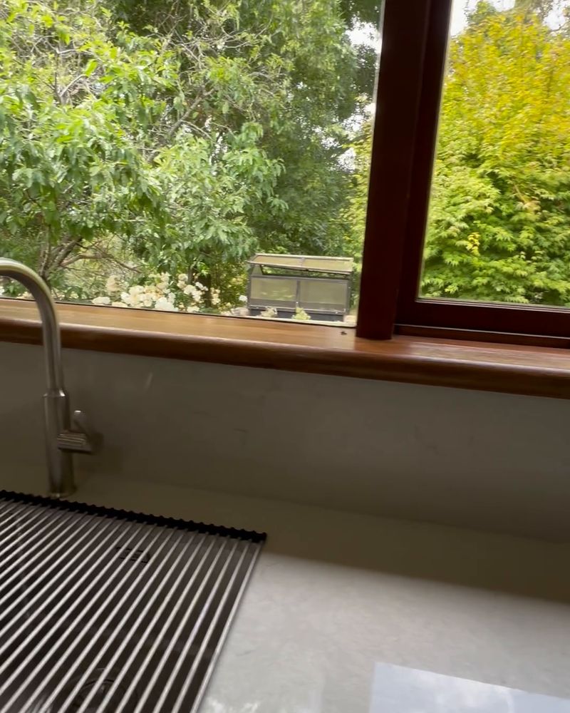 Detail of the gooseneck tap and sink with the garden through the timber-framed window