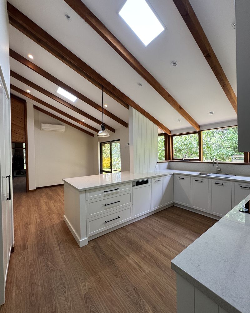The whole kitchen beneath a raked ceiling of exposed timber beams and a skylight, with the island and white shaker cabinetry
