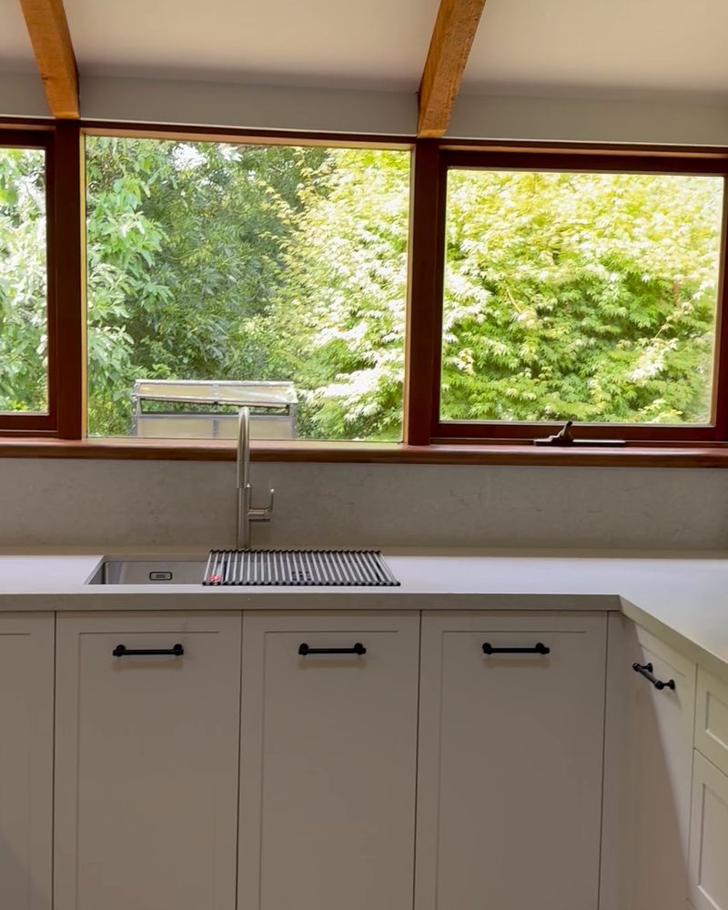 Undermount sink and gooseneck tap beneath timber-framed windows, with white shaker cabinetry and black bar handles