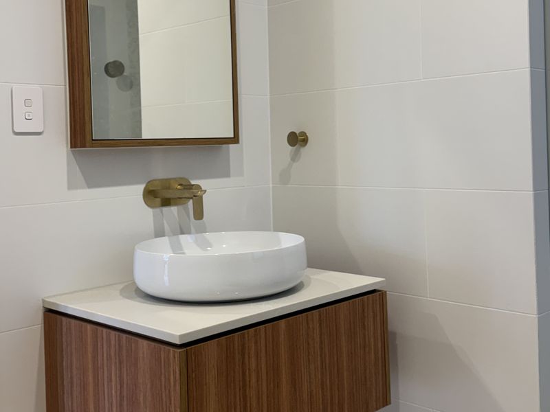 Wall-hung timber vanity with a round white basin, brushed brass wall tap and timber-framed mirror