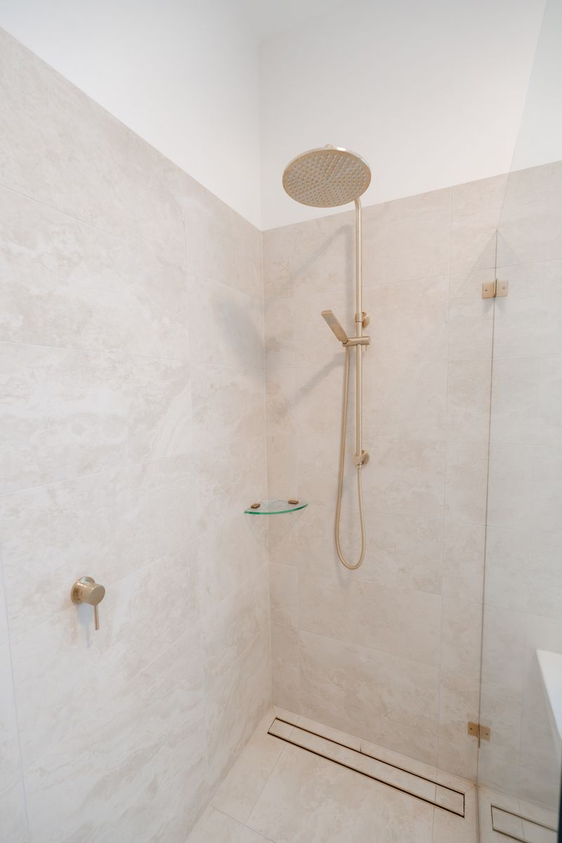 Walk-in shower with floor-to-ceiling tiles and a brass rain shower head