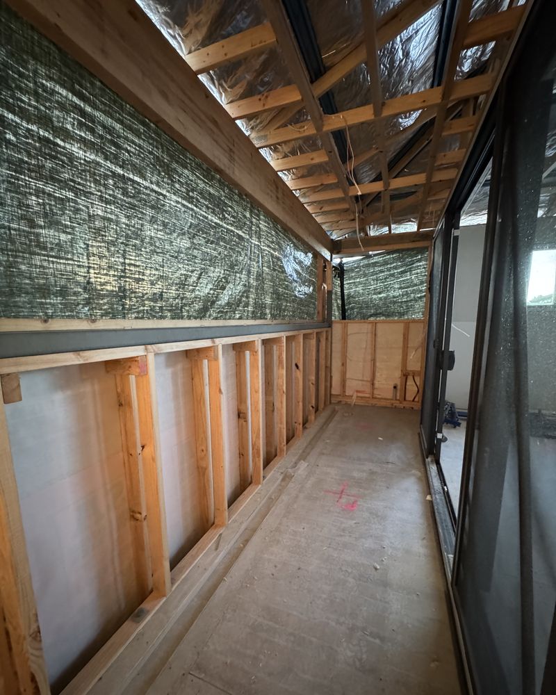 An upper level closed in, with foil-faced wrap, framed walls and black-framed sliding doors