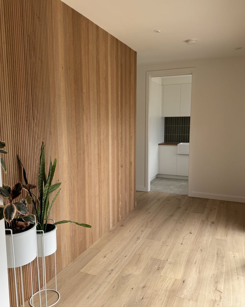 A full-height feature wall of vertical timber battens running the length of a hallway, with wide oak floorboards and two white planters